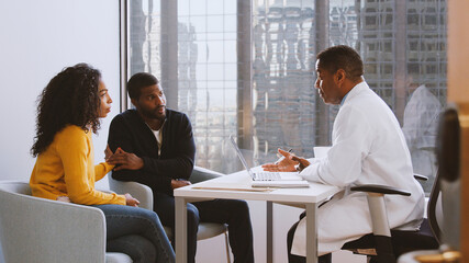 Worried Couple Having Consultation With Male Doctor In Hospital Office