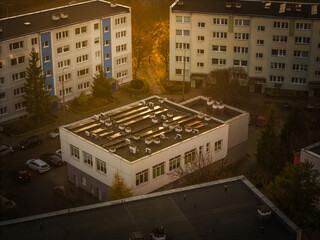 Aerial view of a compact building with multiple roof-mounted units nestled among taller residential buildings, bathed in the warm glow of the setting sun, Gdansk, pomorskie, Poland.