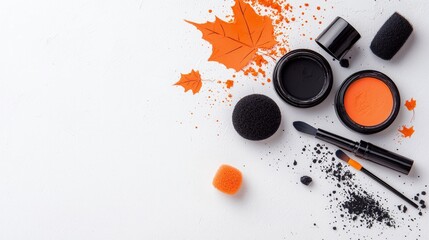 Overhead view of Halloween-themed makeup supplies including orange and black face paints, sponges, brushes, and decorative autumn leaves.