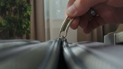 A Macro shot of a hand unzipping a suitcase with a plastic zipper and metal pull tab in a brightly lit room.