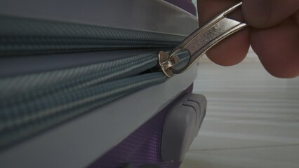 Close-up of a hand unzipping a purple suitcase. Focus on zipper and suitcase detail. Ideal for travel concept.