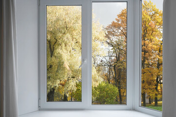  View from the window  on yellow treesin a garden, landscape with autumn forest, window frame.