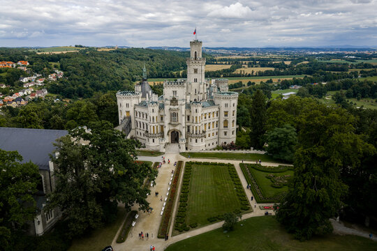 Aerial view of the majestic Zamek Hlubok&aacute; castle, its white facade contrasting against the lush green landscape, a serene vista under a cloudy sky, Hluboka nad Vltavou, Jihocesky kraj, Czechia.