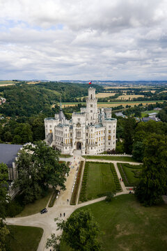 Aerial view of the pristine white Hlubok&aacute; Castle rises majestically amidst verdant gardens and rolling hills under a vast sky, Hluboka nad Vltavou, Jihocesky kraj, Czechia.
