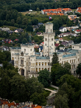 Aerial view of a majestic white castle with intricate turrets and towers nestled amidst lush greenery, a striking contrast against the red rooftops, Hluboka nad Vltavou, Jihocesky kraj, Czechia.