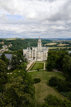 Aerial view of the majestic Zamek Hlubok&aacute; castle's white facade contrasts with the lush green lawns and surrounding verdant forests under a cloudy sky, Hluboka nad Vltavou, Jihocesky kraj, Czechia.