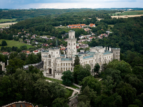 Aerial view of the striking Zamek Hluboka castle, a vision in white stone amidst verdant trees under a soft sky, Hluboka nad Vltavou, Jihocesky kraj, Czechia.