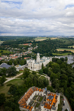 Aerial view of the stark white Zamek castle, a beacon amidst the verdant landscape, its intricate architecture contrasting with the soft, rolling hills, Hluboka nad Vltavou, Jihocesky kraj, Czechia.