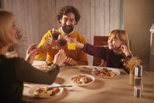 Three family members share a joyful moment at a dinner table filled with tasty autumn dishes. Laughter and clinking glasses create a warm, inviting atmosphere.
