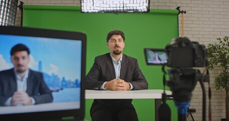 A live streaming studio setup with a camera, monitor, and green screen, showcasing a professional environment. A man in a suit presents information or news. Ideal for media production.