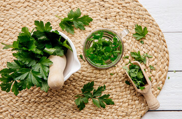 Above view of homemade herbal medicinal tea made from parsley Petroselinum crispum. Green leaves in tea cup on white wood background with fresh leaves in mortar and pestle.