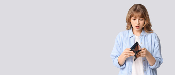 Sad young woman with empty wallet on grey background