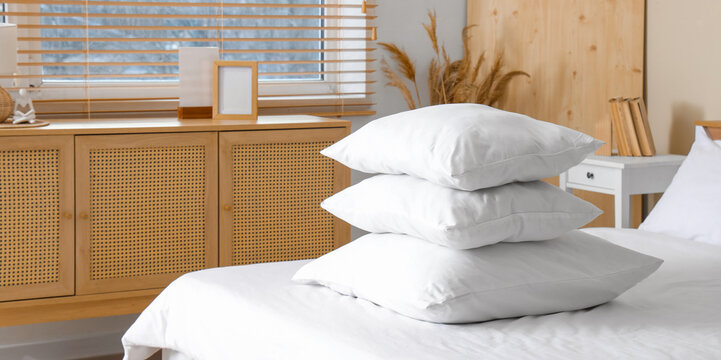 Cozy bed with white blanket and stack of soft pillows in stylish bedroom, closeup