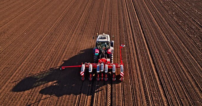 Tractor planting seeds in a vast plowed field under a cloudy sky
