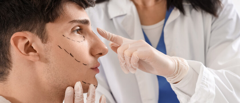Young man with marked face visiting plastic surgeon in clinic, closeup