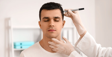 Doctor marking young man's head with hair loss problem in clinic, closeup