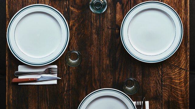Rustic wooden table setting with white oval plates and silverware