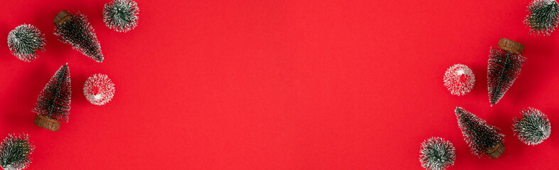 A festive Christmas banner background with a flat layout: miniature snow-covered pine trees create a frame on a bright red background with plenty of room for text.