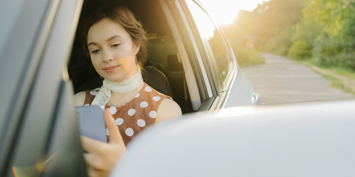Smiling woman in vintage polka dot dress and straw hat sitting in driver’s seat and talking on video call via smartphone. Retro lifestyle mix of elegance, travel, and modern connection.