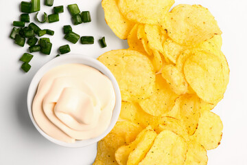 Bowl of tasty sour cream with sliced green onion and potato chips on white background