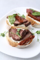 Bruschettas with roast beef, cream cheese, basil and sun-dried tomatoes on table, closeup