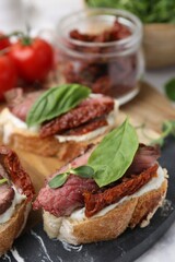 Bruschettas with roast beef, cream cheese, basil, sun-dried tomatoes and fresh vegetables on table, closeup