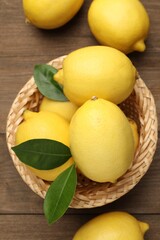 Fresh lemons with green leaves and wicker basket on wooden table, flat lay