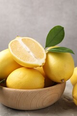 Whole, cut lemons with green leaves and bowl on grey textured table, closeup