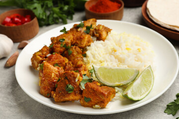 Delicious chicken tikka masala with rice, parsley and lime on grey textured table, closeup