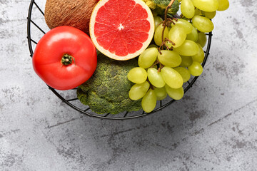 Basket with different fresh fruits and vegetables on grey background, closeup