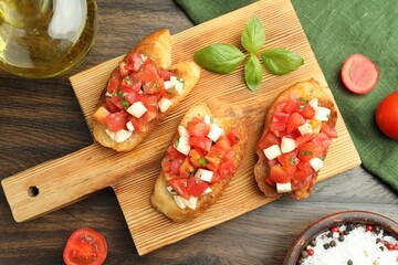 Tasty bruschettas with tomatoes, mozzarella cheese and basil served on wooden table, flat lay