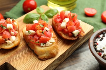 Tasty bruschettas with tomatoes, mozzarella cheese and basil served on wooden table, closeup