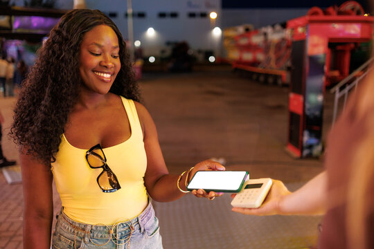 Smiling woman making a contactless payment with her smartphone at a night fair