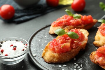 Tasty bruschettas with tomatoes and basil served on black table, closeup