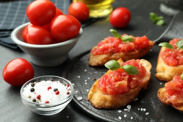 Tasty bruschettas with tomatoes and basil served on black table, closeup