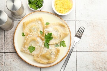 Delicious ravioli with cheese and parsley served on light tiled table, flat lay