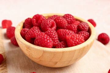 Wooden bowl with fresh raspberries on light background