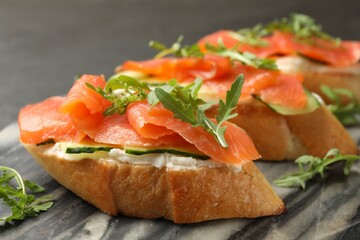 Tasty bruschettas with salmon, cream cheese, cucumber and arugula on table, closeup