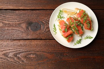 Tasty bruschettas with salmon, cream cheese, cucumber, arugula and lemon on wooden table, top view. Space for text
