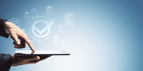 Businessman using tablet with digital checklists and approval icons on light blue abstract background for digital quality assurance concept.