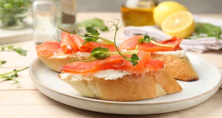 Tasty bruschettas with salmon, cream cheese and microgreens on wooden table, closeup
