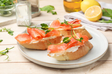 Tasty bruschettas with salmon, cream cheese and microgreens on wooden table, closeup