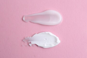 Samples of moisturizing creams on pink background, top view