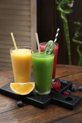 Different tasty smoothies in glasses and ingredients on wooden table, closeup