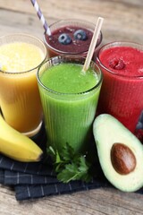 Different tasty smoothies in glasses and ingredients on wooden table, closeup