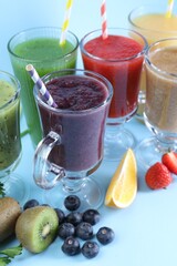 Different tasty smoothies in glasses and ingredients on light blue background, closeup