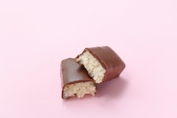 Halves of tasty chocolate covered coconut candy on pink background