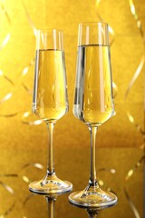 New Year celebration. Sparkling wine in flute glasses and serpentine streamers against shiny golden background