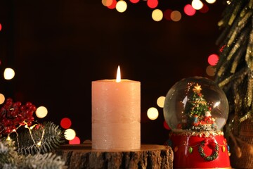 Burning candle and Christmas decor on table against dark background with blurred lights, closeup. Bokeh effect