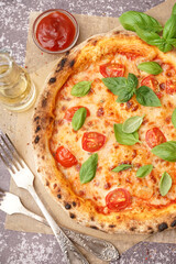 Baking paper with tasty pizza Margarita and basil on dark table